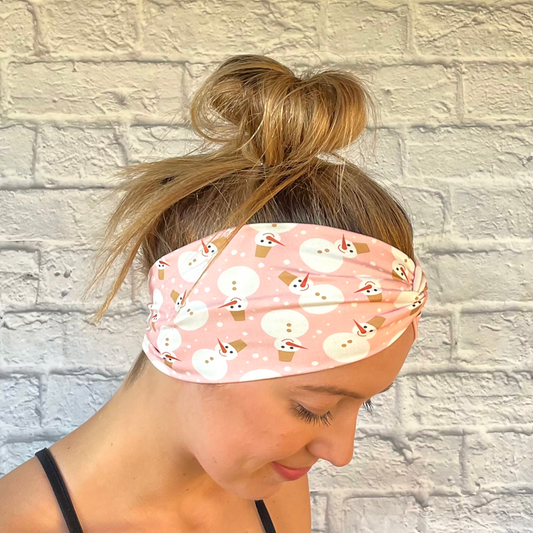 Woman with hair in bun wearing wide, twisted, pink headband with snowman print.