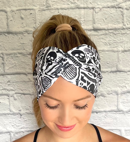 Woman with hair in curled ponytail wearing white, wide twist headband with black skeleton print. 