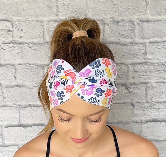 Woman with hair in curled ponytail wearing wide, twisted headband in white with multi-color dog paw print.