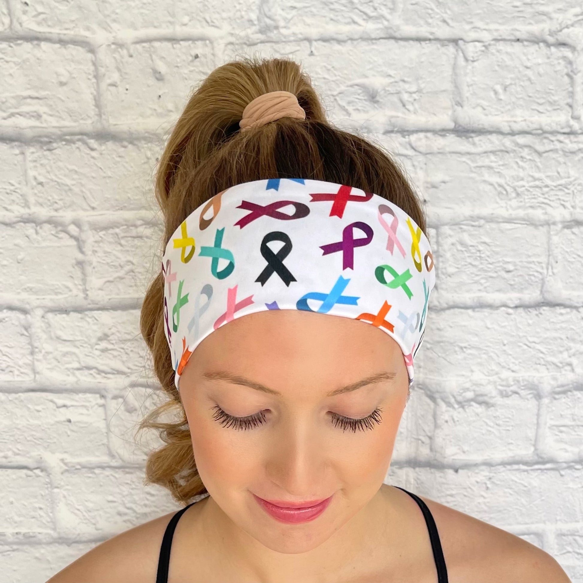 Woman with hair in curled ponytail wearing white, stretchy headband with ribbon print in varying color ribbons.