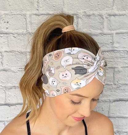 Woman with hair in curled ponytail wearing wide, twisted, sage green color headband with cat print.