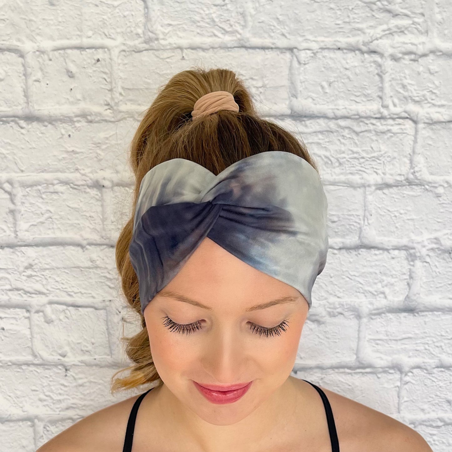 Woman with hair in ponytail wearing white, gray, and blue wide twist headband.