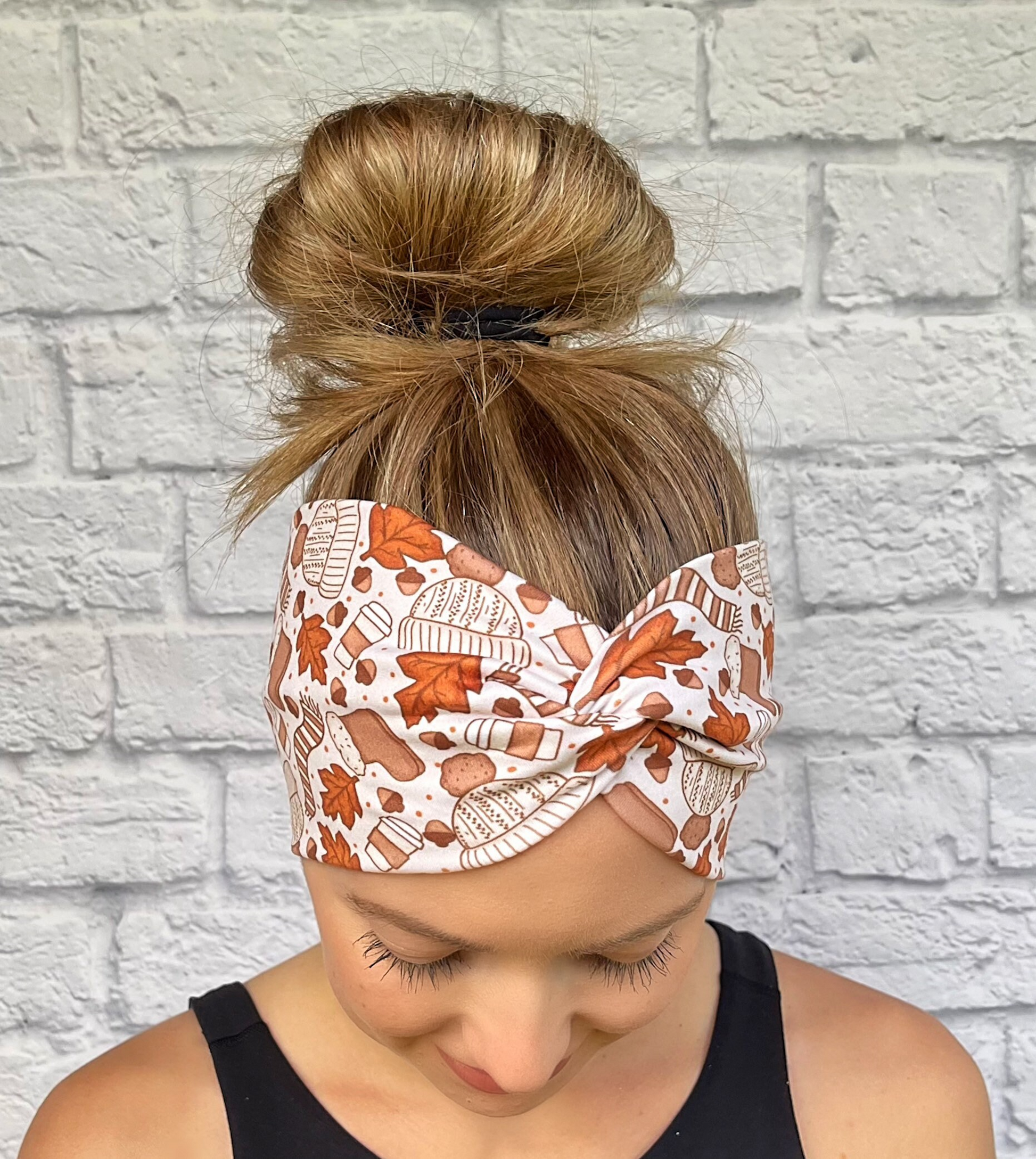 Woman with hair in bun wearing wide, twisted headband in light brown with leaves, coffee, hats, and gloves print.