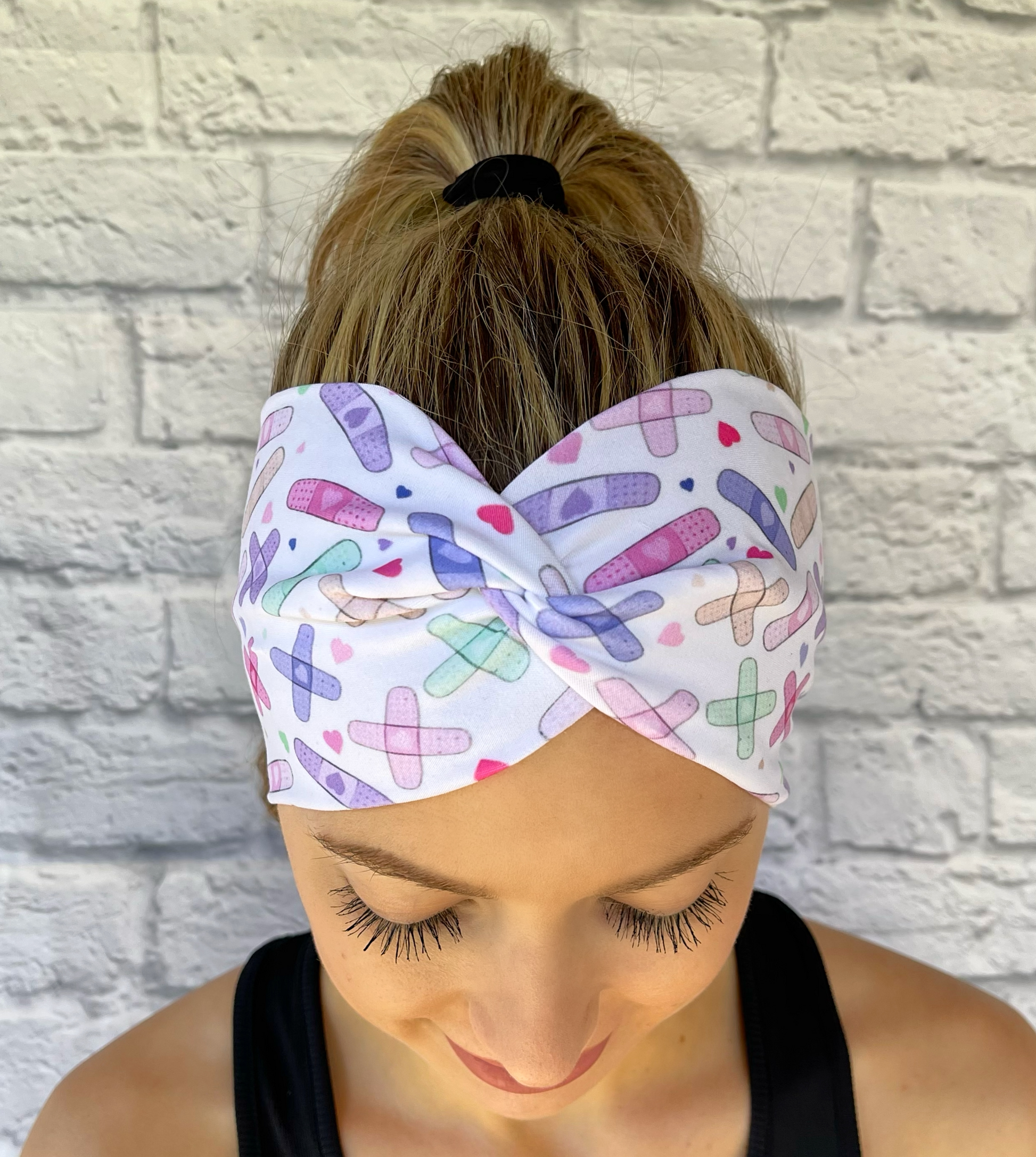 Woman with hair in curled ponytail wearing wide, white, twisted headband with pastel bandage print.