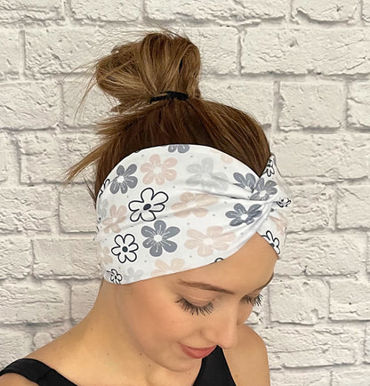 Woman with hair in bun wearing wide, twisted, white headband with floral print in light pink, gray, and black.