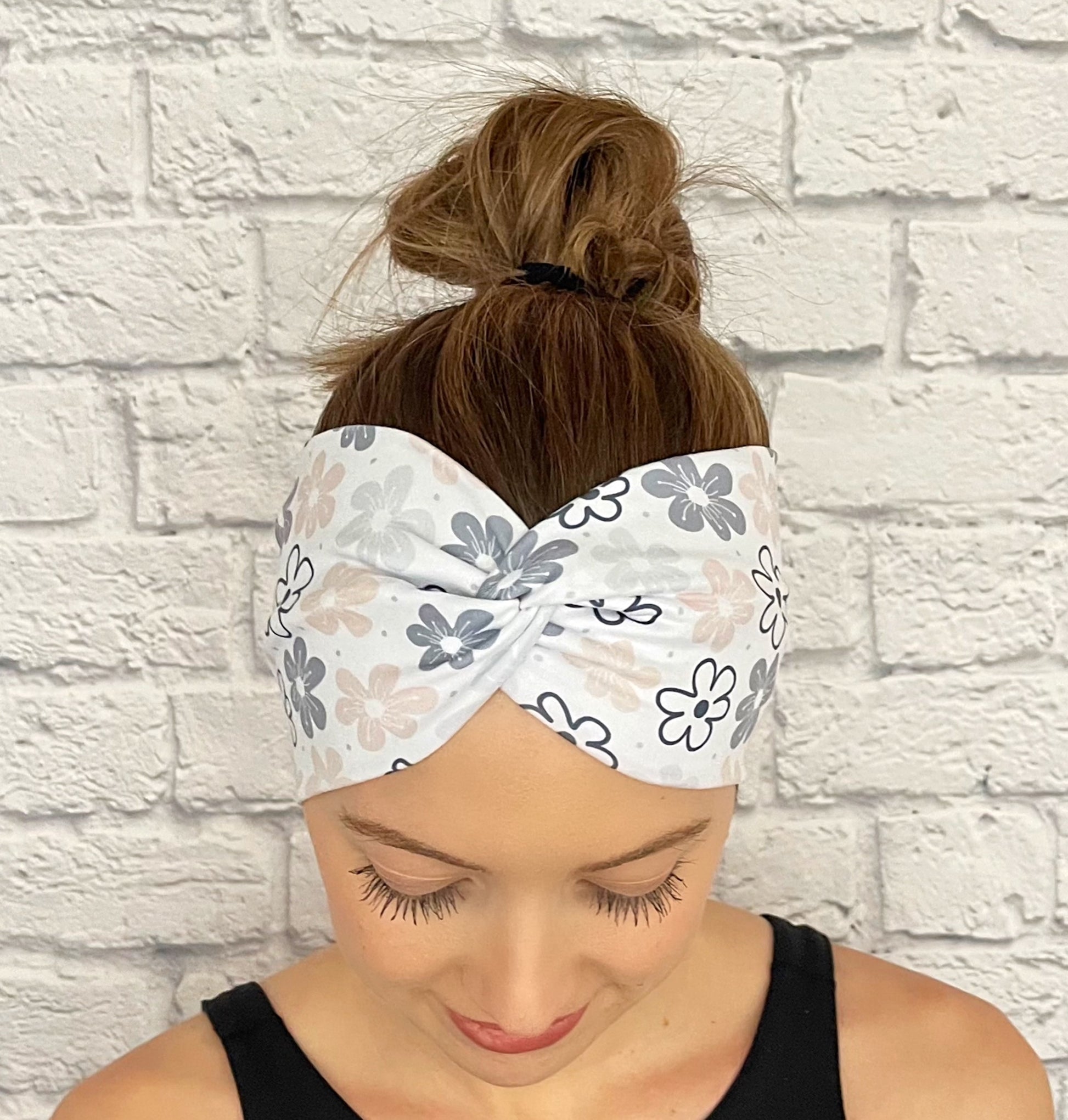 Woman with hair in bun wearing wide, twisted, white headband with floral print in light pink, gray, and black.