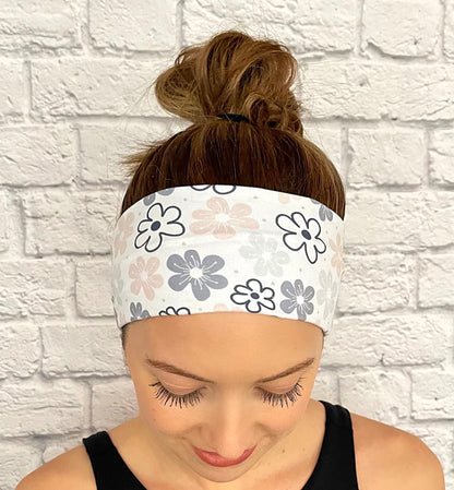 Woman with hair in bun wearing flat, stretchy headband in white with light pink, gray, and black floral print.