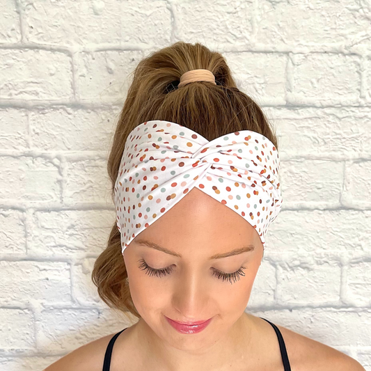 Woman with hair in ponytail wearing wide, twisted, white headband with multi-color small polka dots.