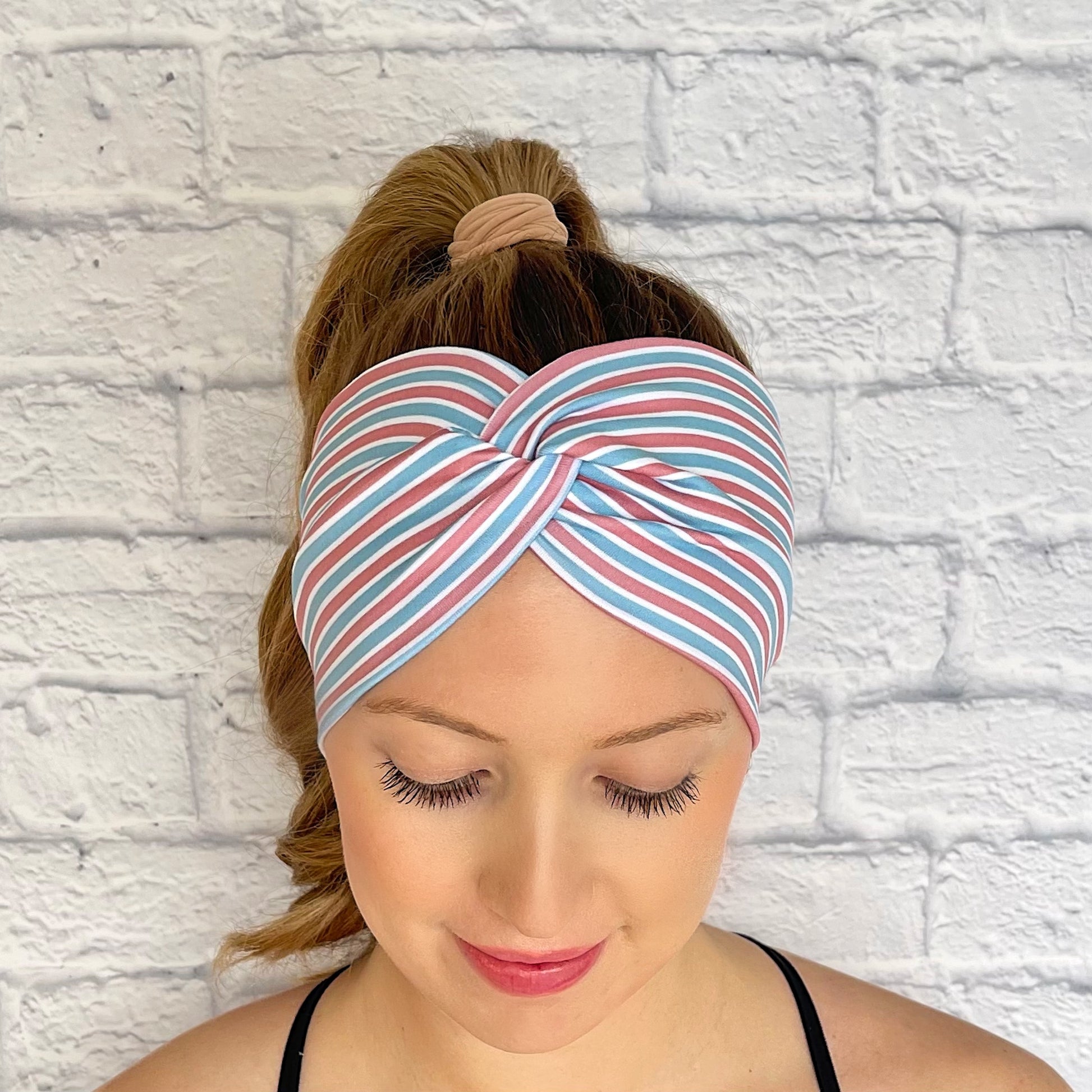 Woman with hair in curled ponytail wearing wide, twisted headband with pink, blue, and white, stripe print.