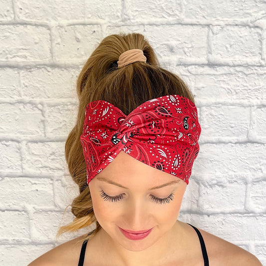 Woman with hair in curled ponytail wearing wide, twisted headband with red bandana print.