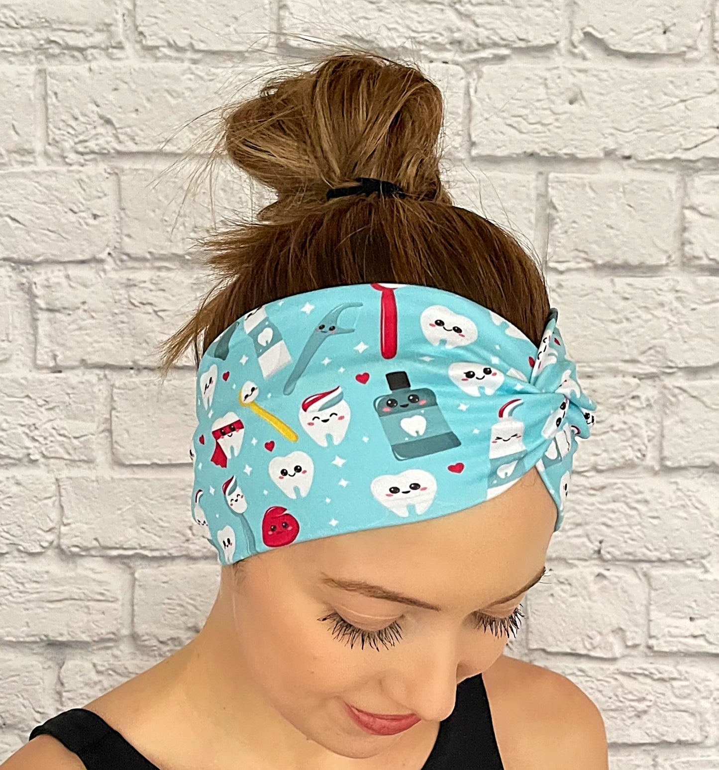 Woman with hair in bun wearing wide, twisted headband in light blue with dental theme print.