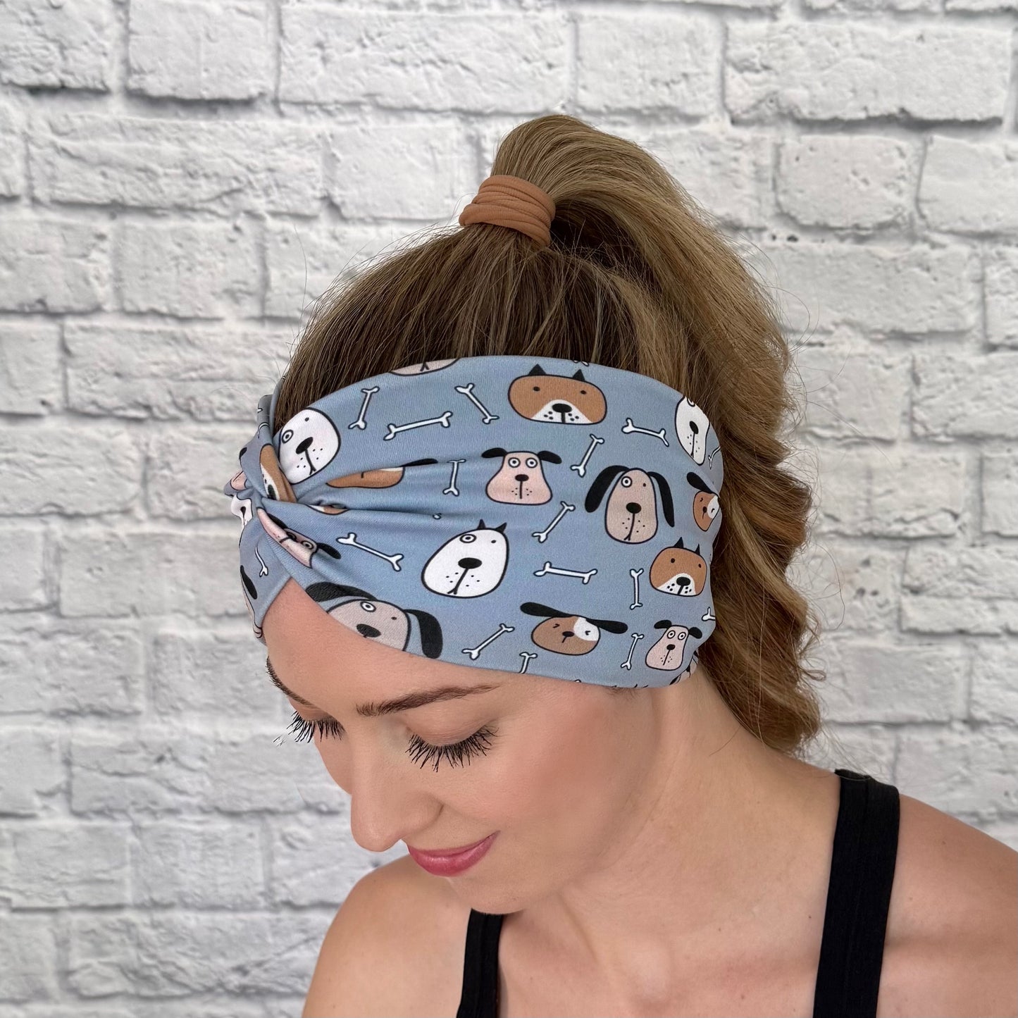 Woman with hair in ponytail wearing wide, twisted headband in blue with dog print.
