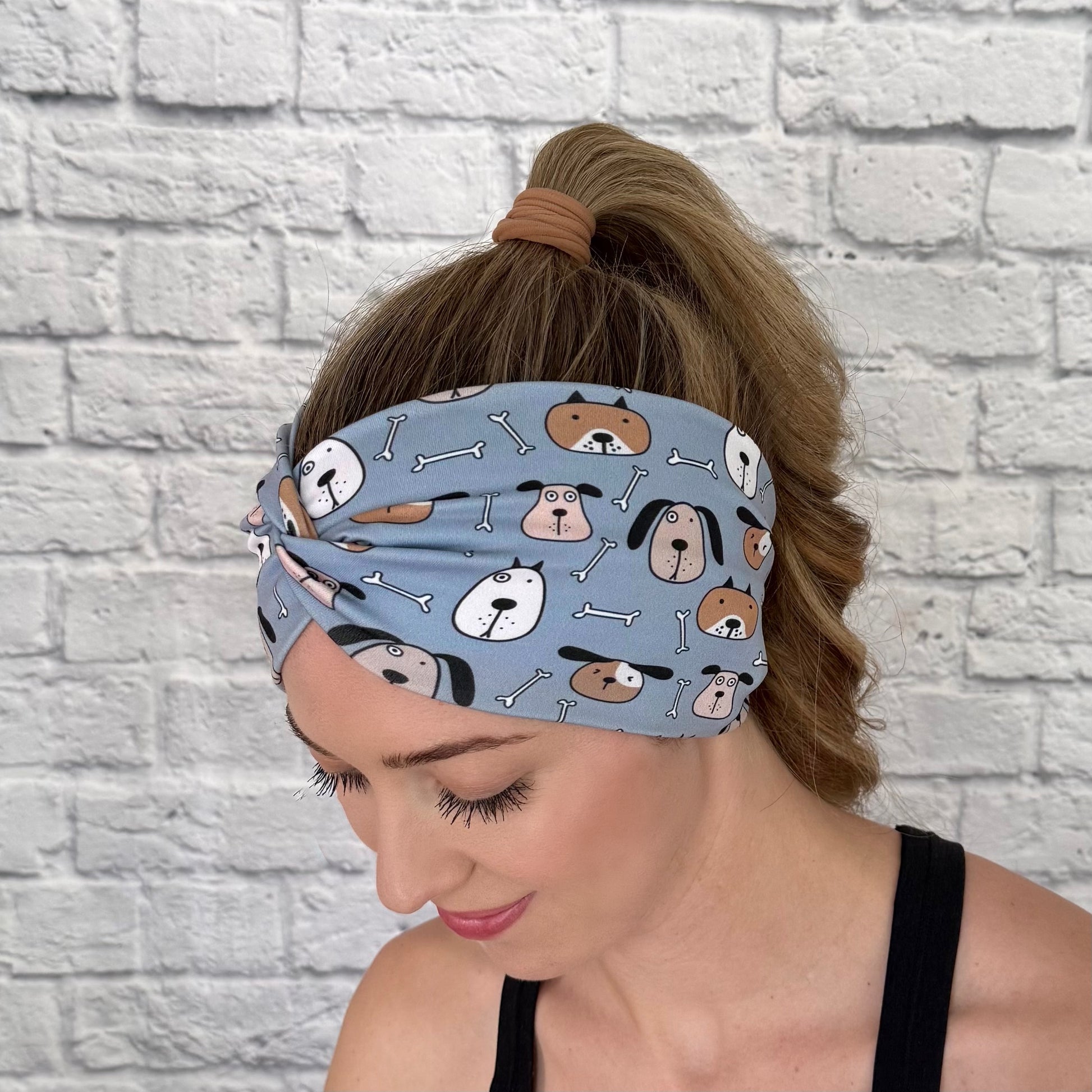 Woman with hair in ponytail wearing wide, twisted headband in blue with dog print.