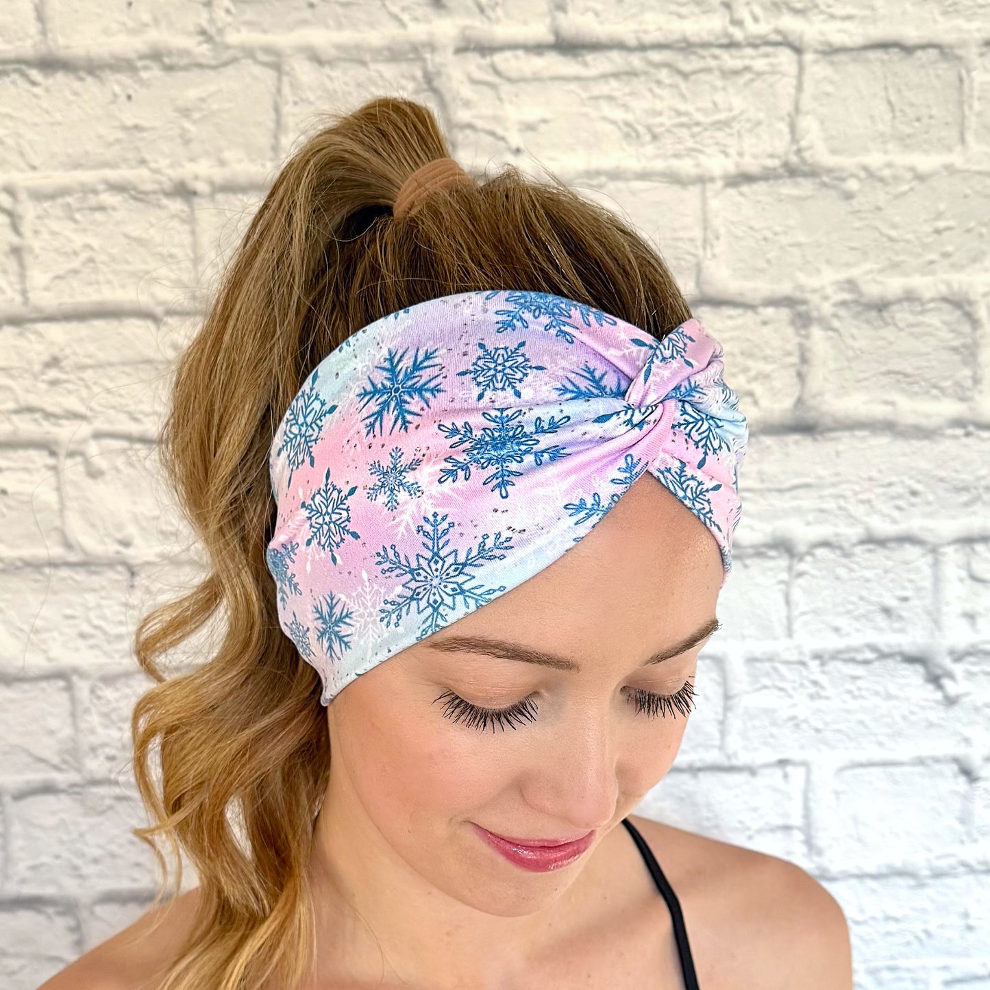 Woman wearing wide, twisted headband with blue, purple, and pink color with blue and white snowflake print.