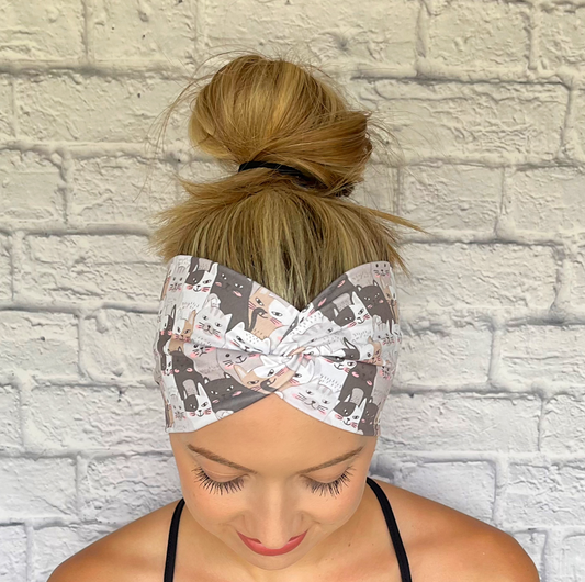 Woman with hair in bun wearing wide, twisted headband in with gray and tan cat print.