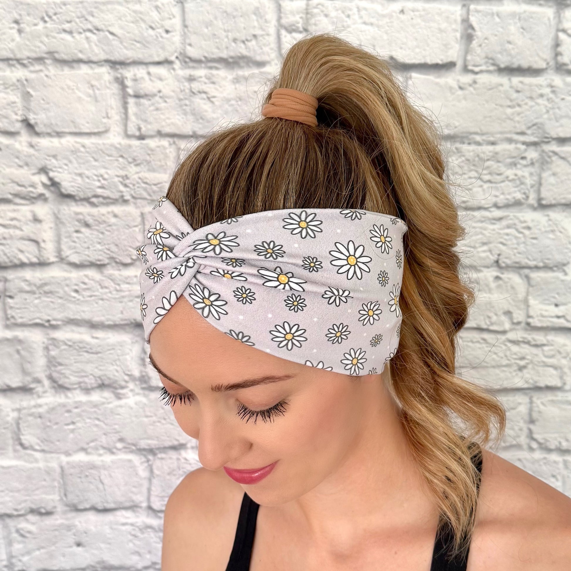 Woman with hair in ponytail wearing wide, twisted headband in gray with white daisy print.