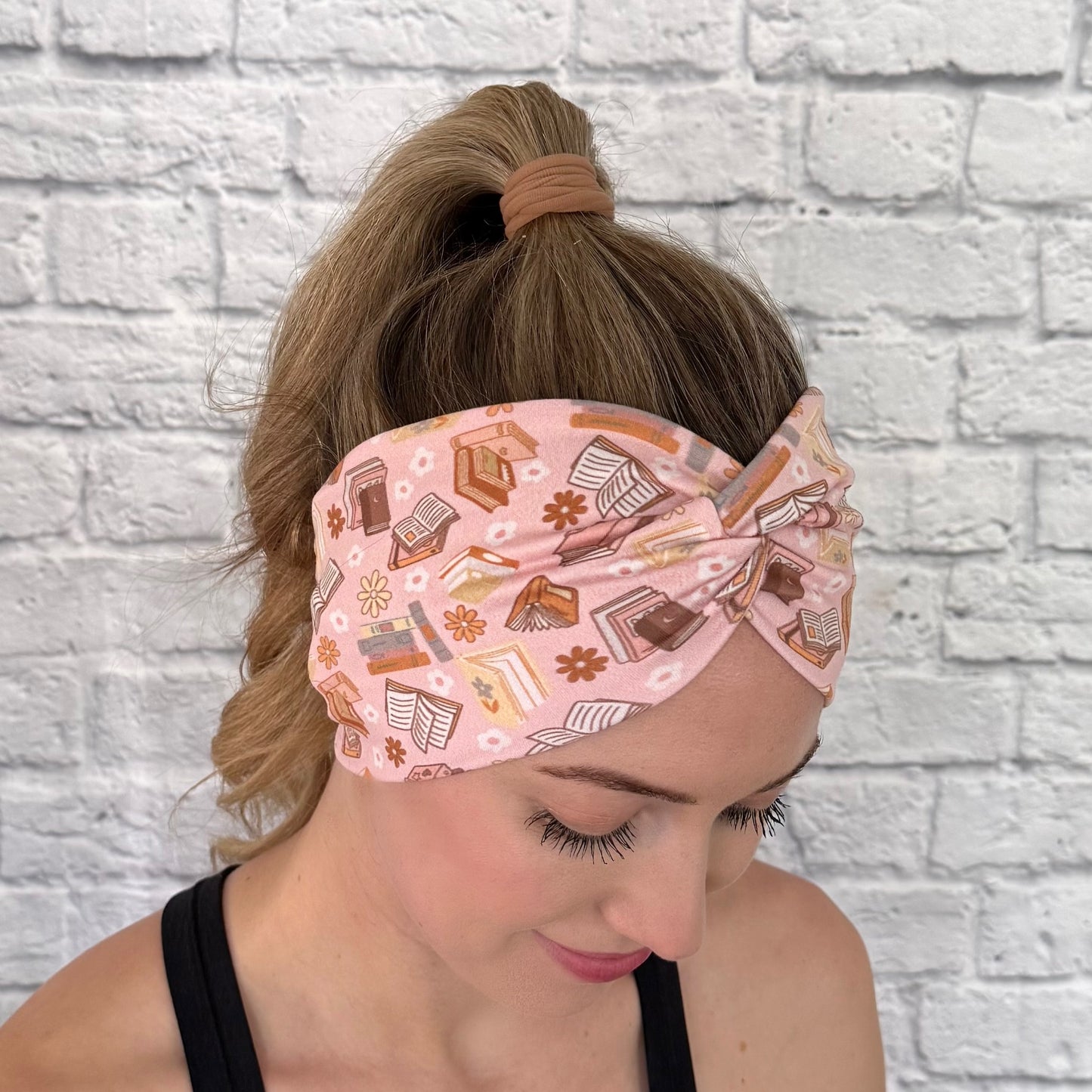 Woman wearing pink, wide twisted headband with books and flower print.
