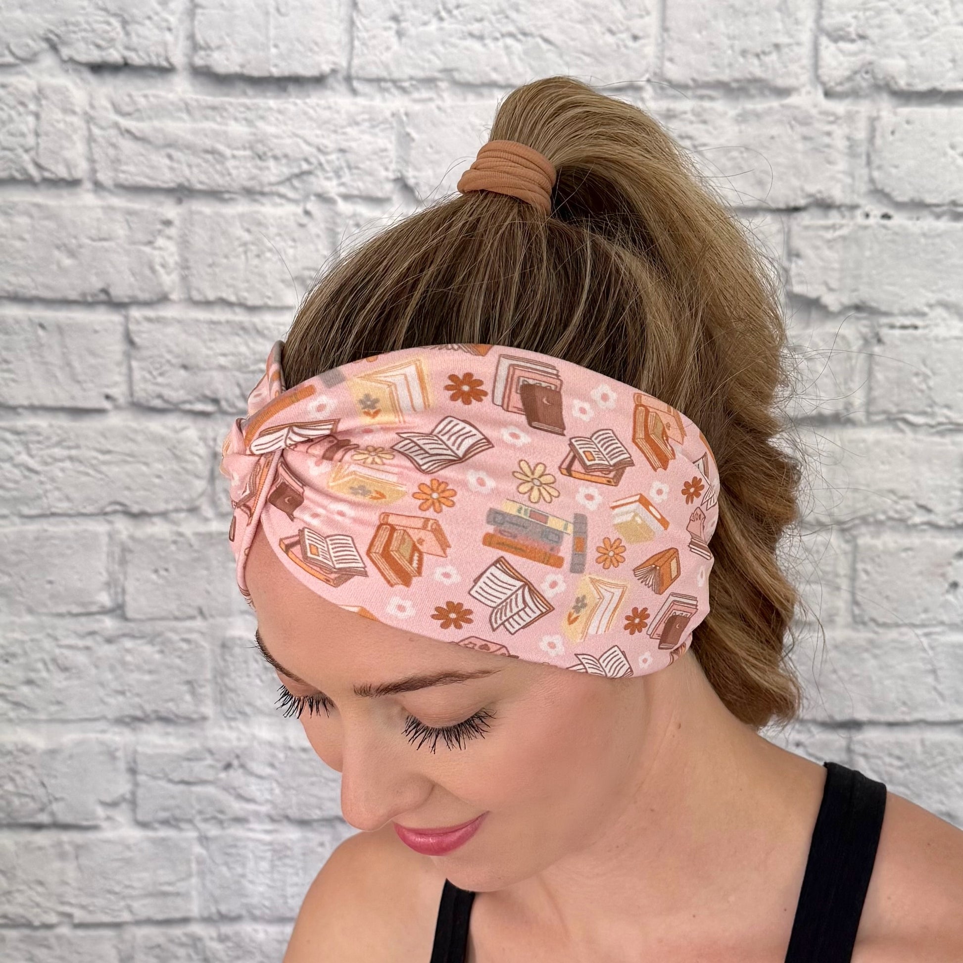 Woman wearing pink, wide twisted headband with books and flower print.