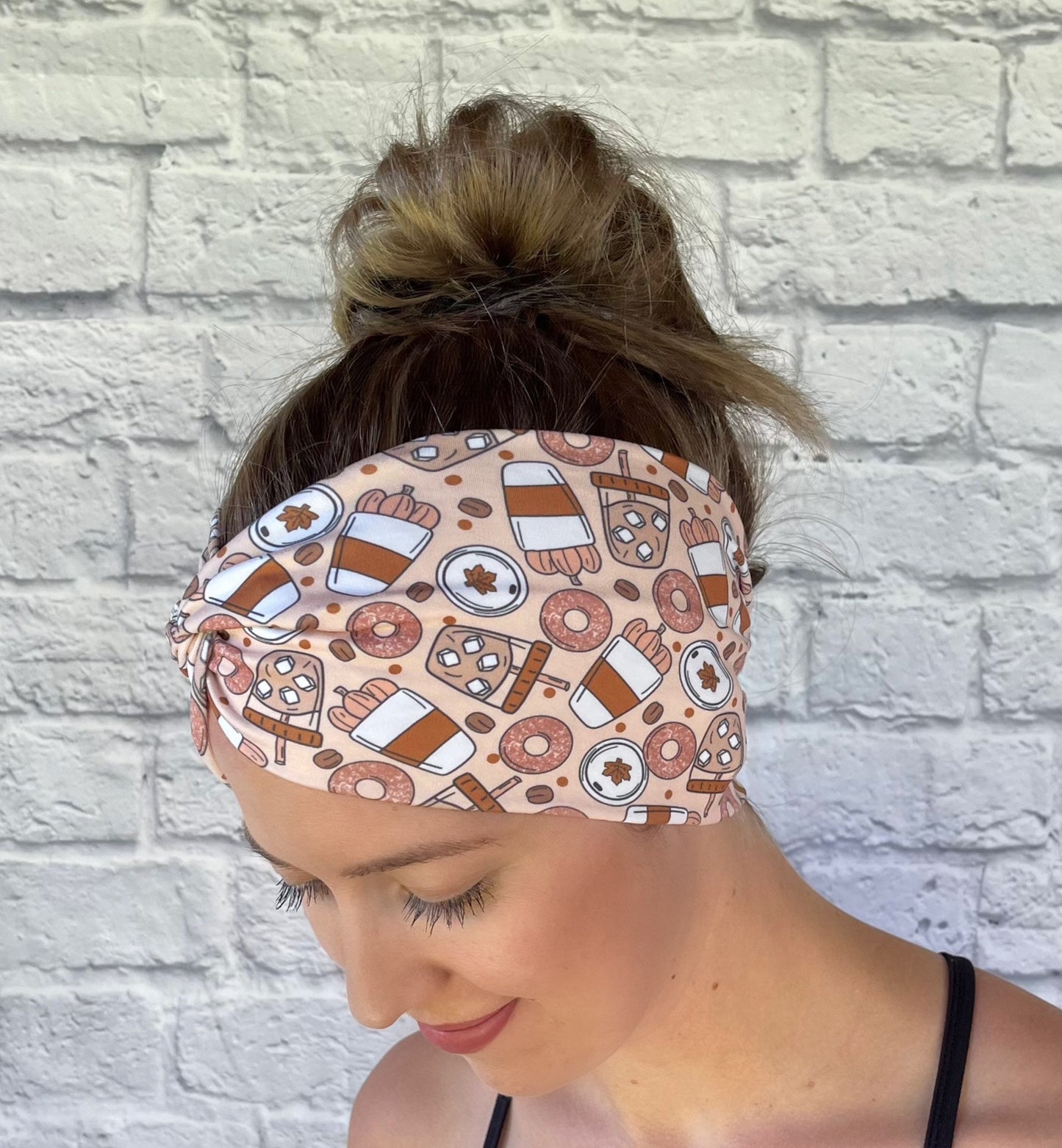 Woman wearing a fall theme, pumpkin spice patterned headband against a white brick wall