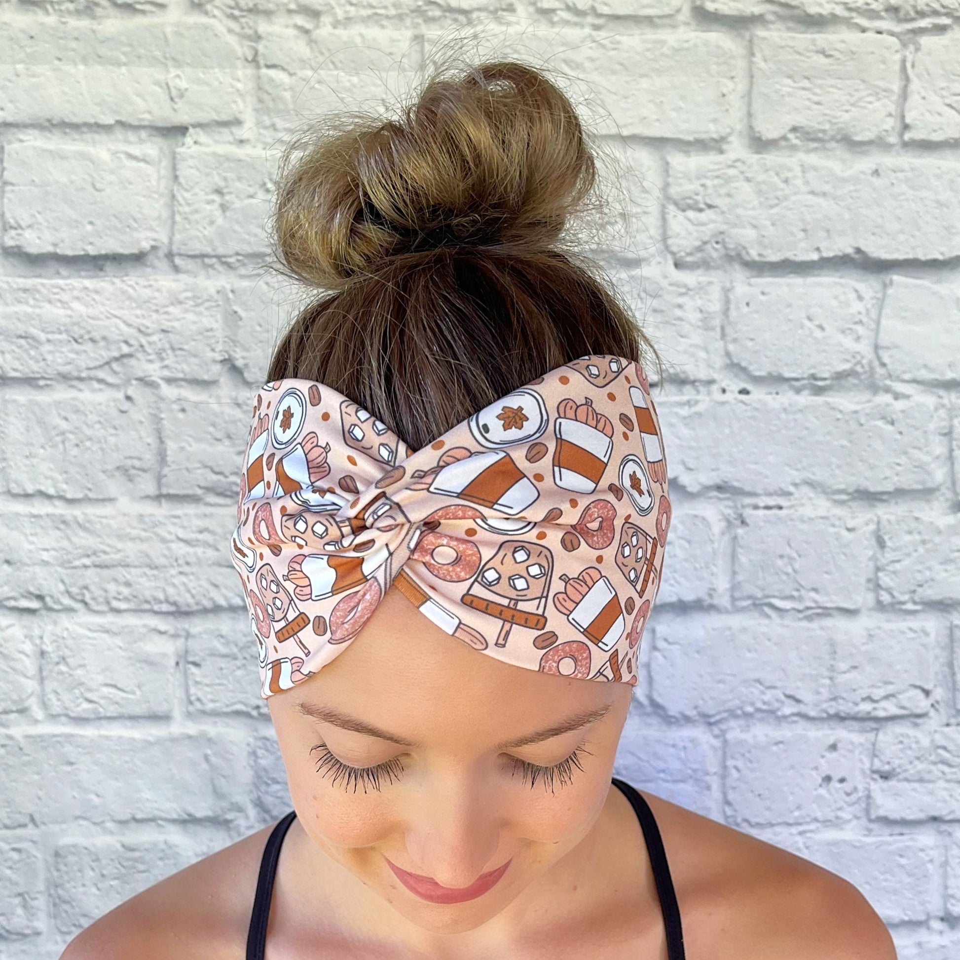 Woman wearing a fall theme, pumpkin spice patterned headband against a white brick wall