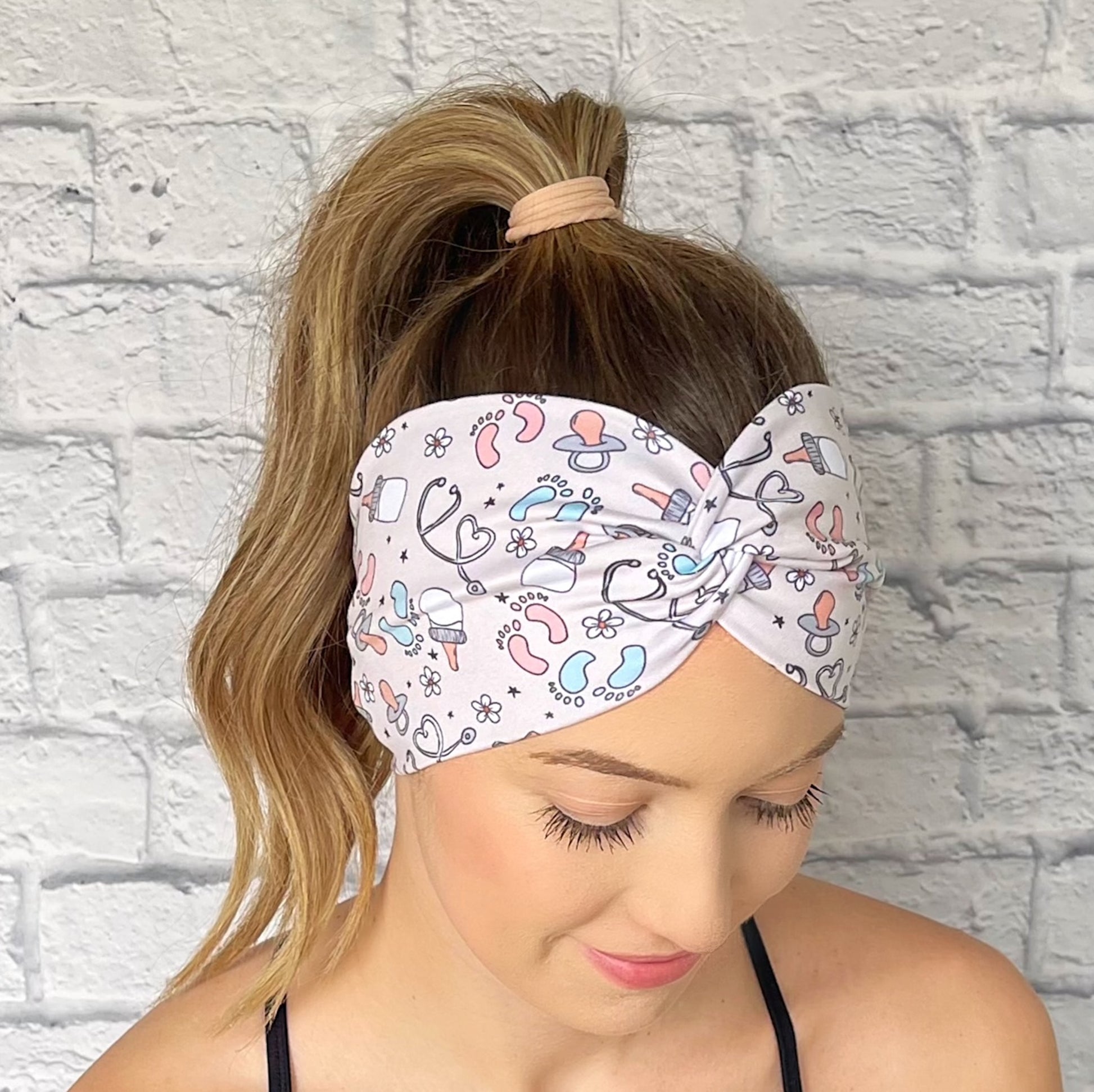 Woman wearing a tan, baby theme patterned headband against a white brick wall.