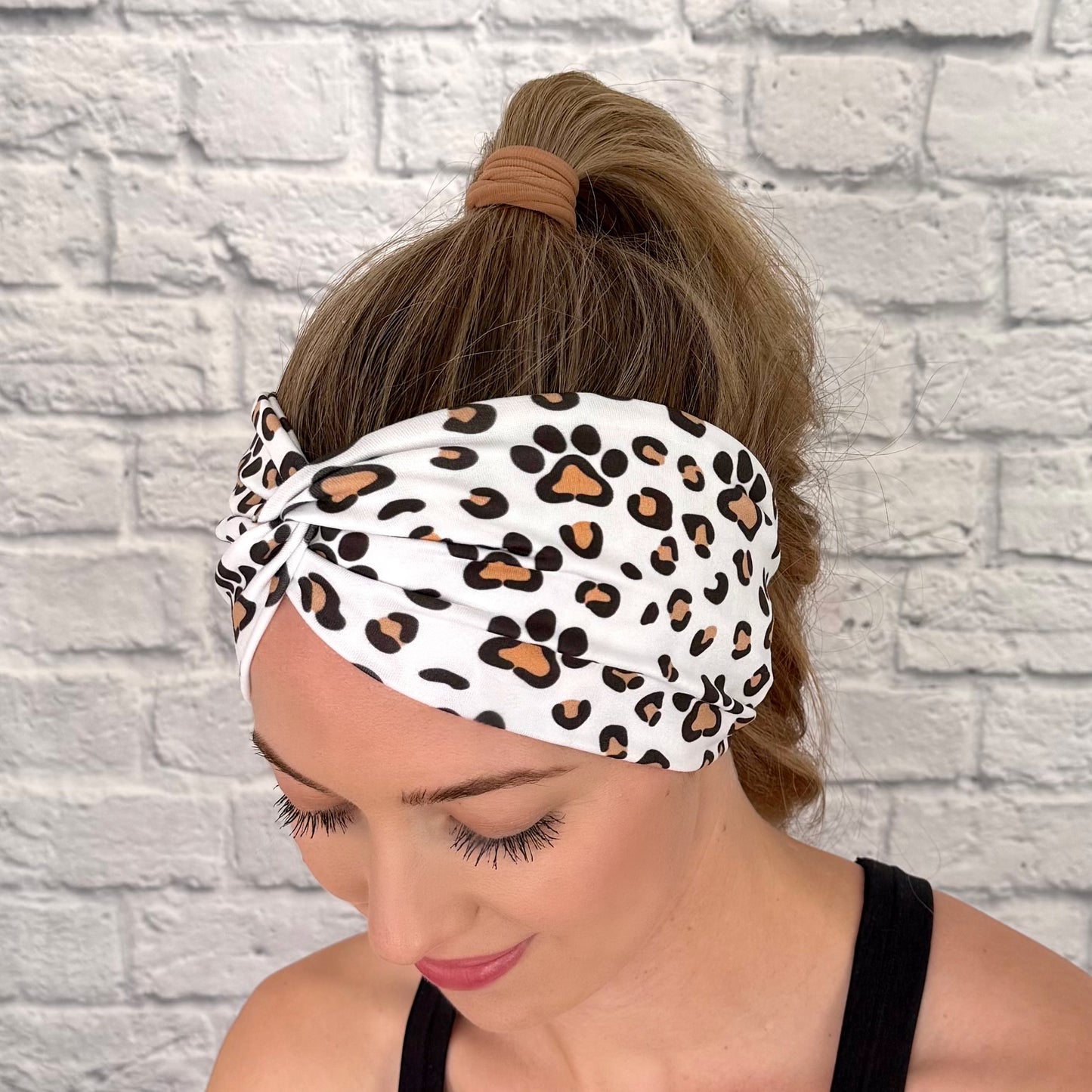 Woman with hair in bun wearing wide, white, twisted headband with brown and black dog paws and cheetah print.
