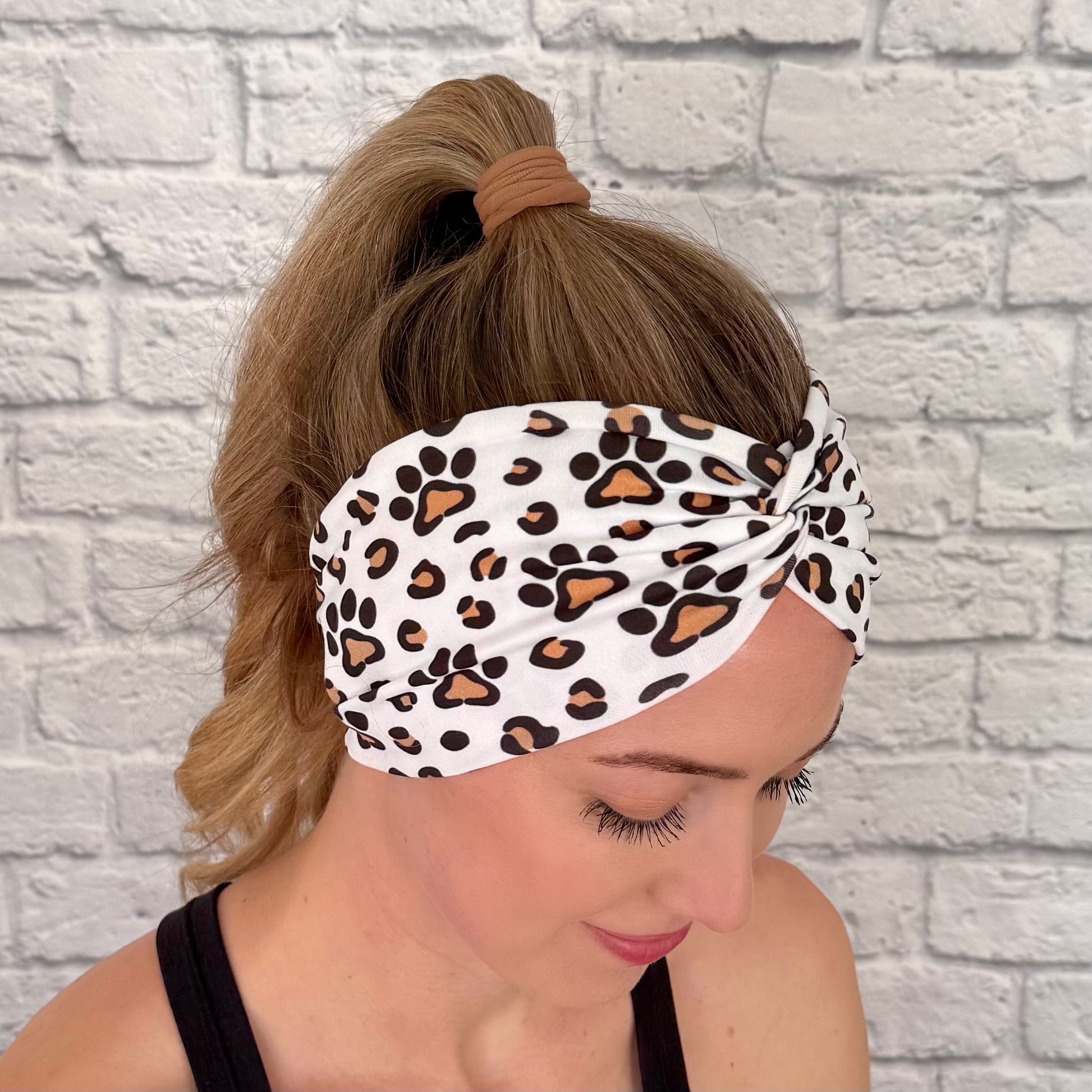 Woman with hair in bun wearing wide, white, twisted headband with brown and black dog paws and cheetah print.