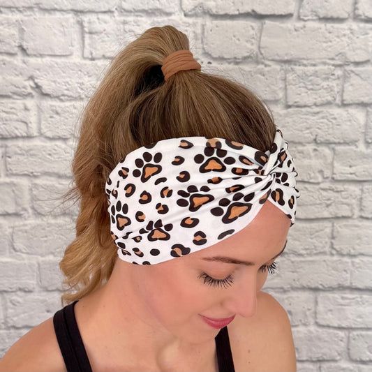 Woman with hair in bun wearing wide, white, twisted headband with brown and black dog paws and cheetah print.