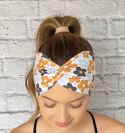 Woman with hair in curled ponytail wearing wide, twisted headband in white with yellow, navy, and light blue floral print.