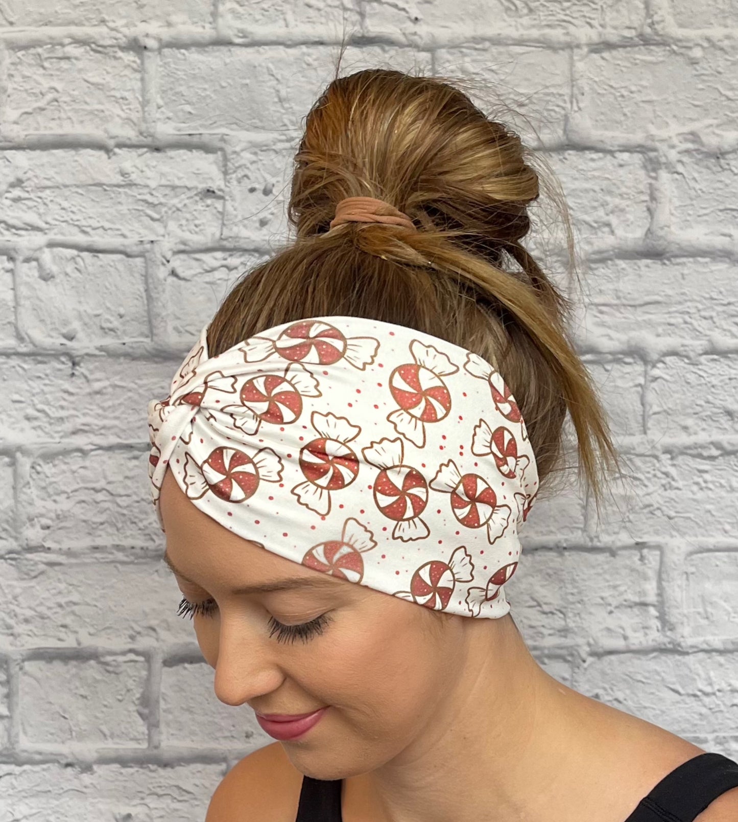 Woman with hair in bun wearing wide, twisted, white headband with red peppermint print.