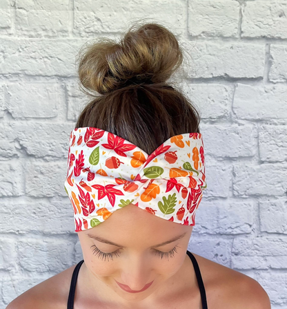 Woman with hair in bun wearing wide, twisted, white headband with red, orange, and green leaves print.