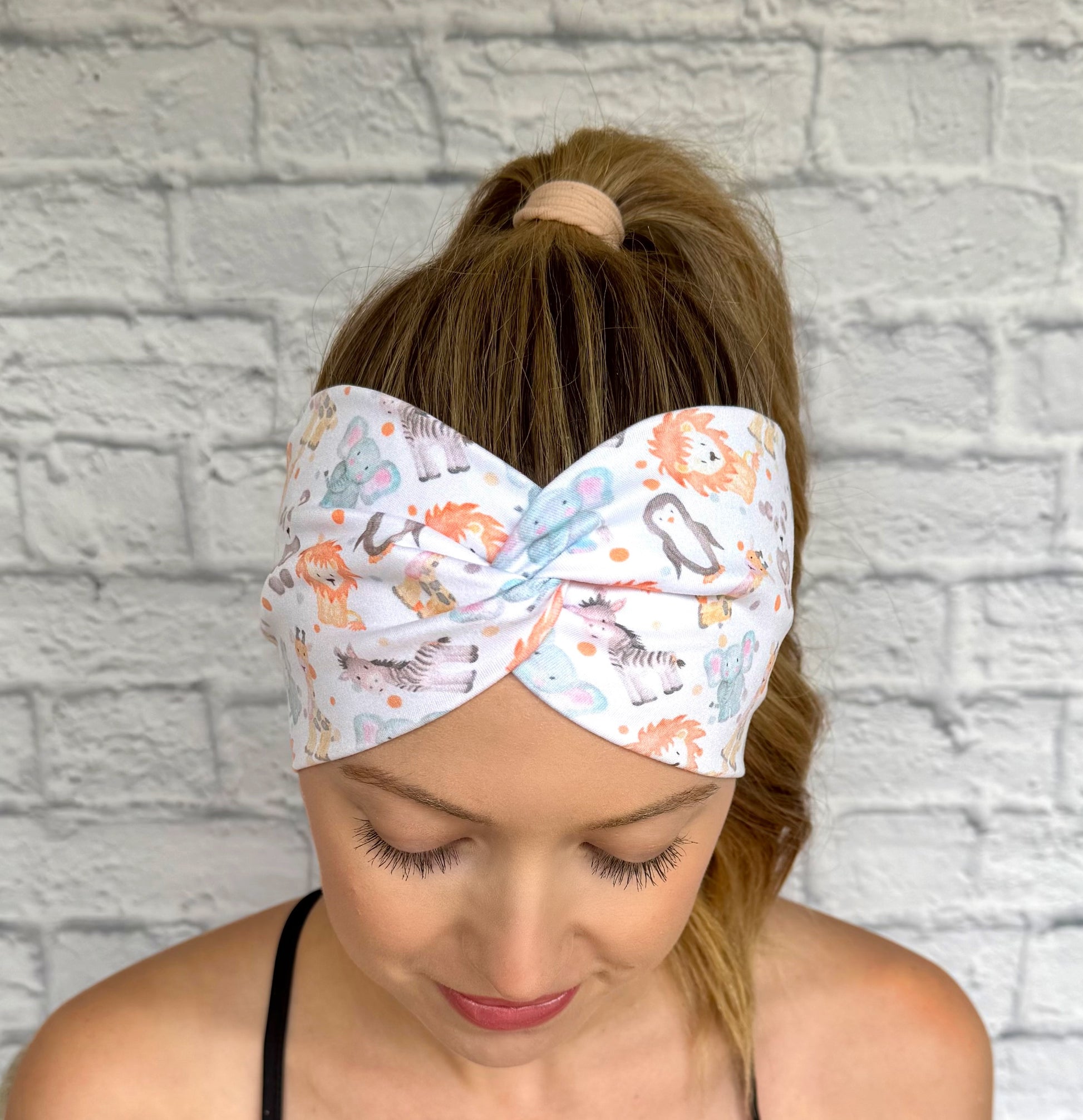 Woman with hair in ponytail wearing wide, twisted headband in white with baby animal and polka dot print.