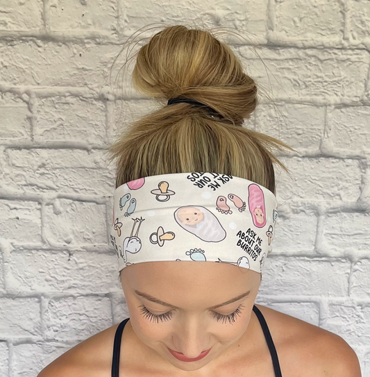 Woman with hair in bun wearing cream color, stretchy headband, with baby theme print and "ask me about our burritos".