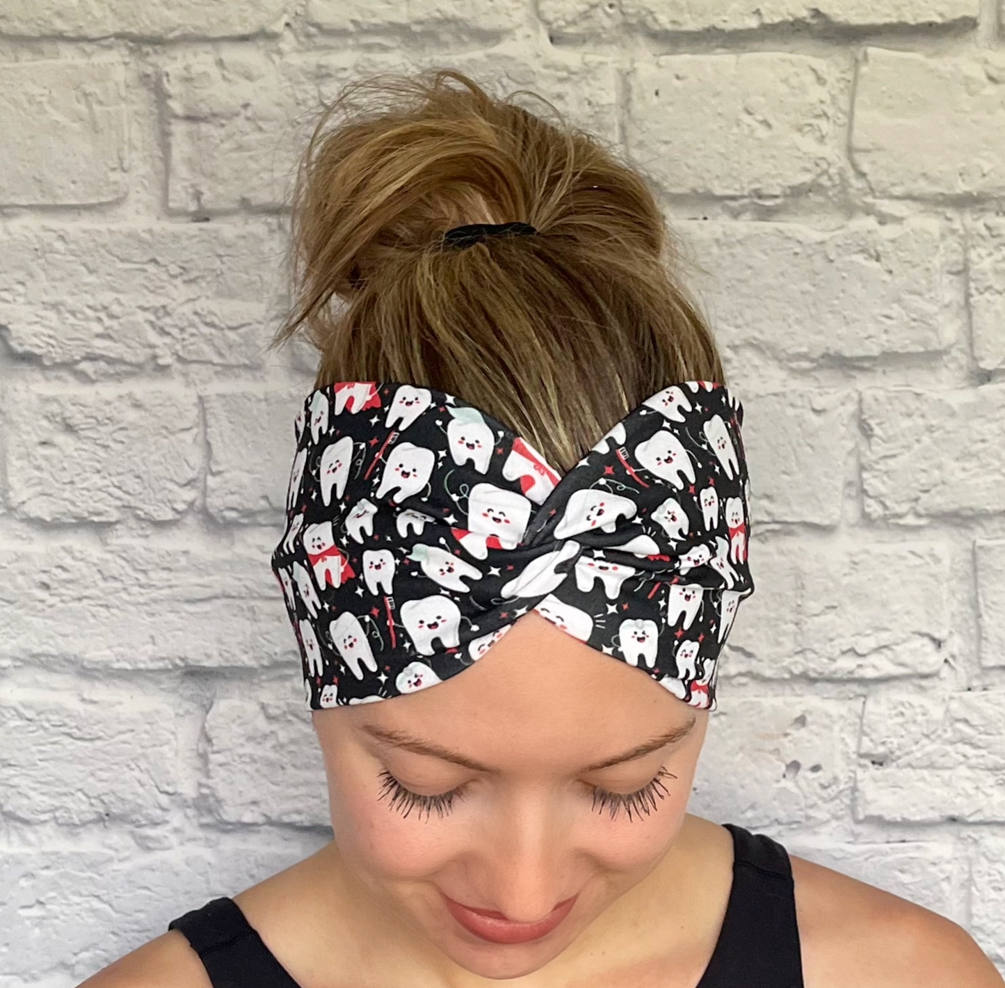 Woman with hair in bun wearing wide, twisted headband in black with white teeth print.