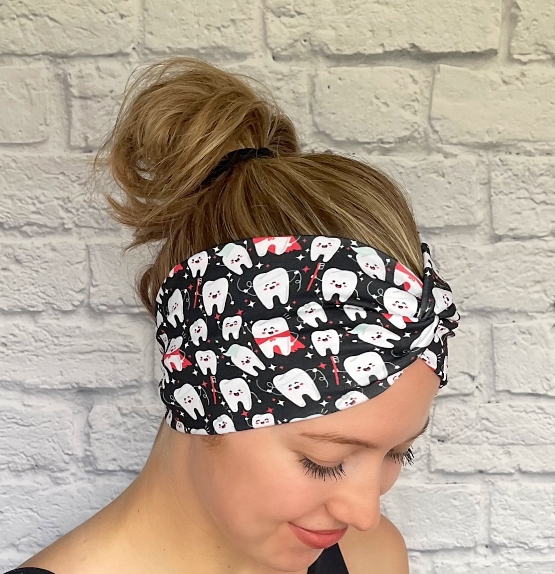 Woman with hair in bun wearing wide, twisted headband in black with white teeth print.