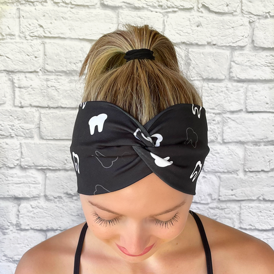 Woman with hair in ponytail wearing wide, black, twisted headband with white teeth print.