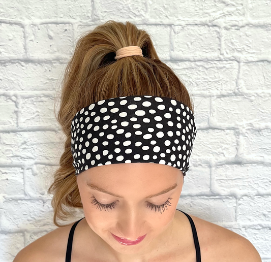 Woman with hair in curled ponytail wearing flat, stretchy headband in black with white polka dot print.