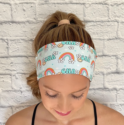 light blue headband with "cna" print, rainbows, white flowers, and smiley faces