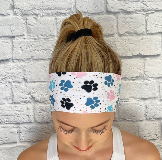 Woman with hair in ponytail wearing flat, stretchy headband in white with blue and pink dog paw print.