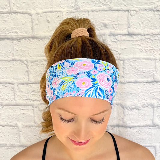 Woman with hair in curled ponytail wearing flat, stretchy headband in bright blue and purple floral print.