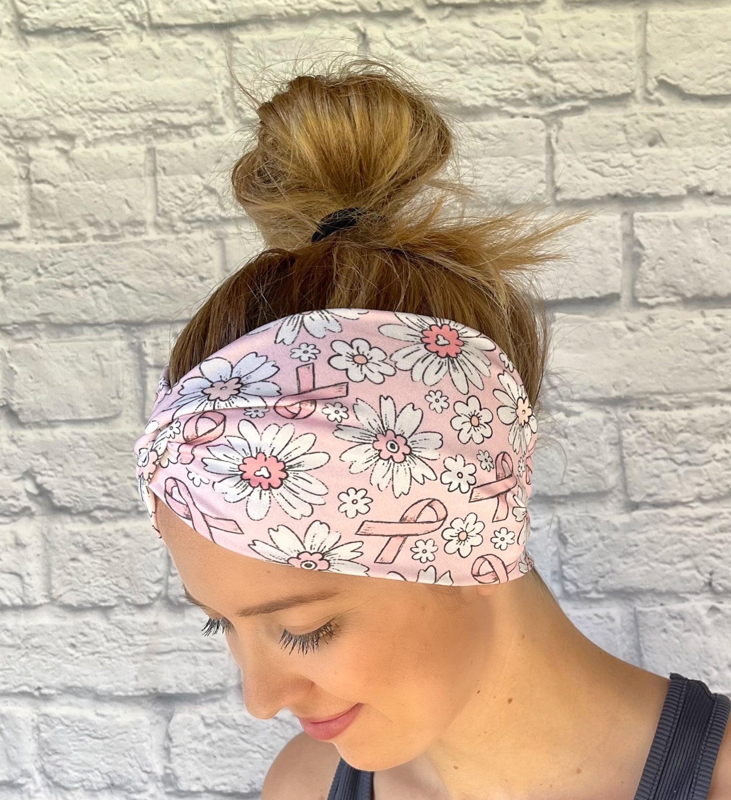 Woman with hair in bun wearing light pink, wide, twisted headband with pink ribbon and white flower print.