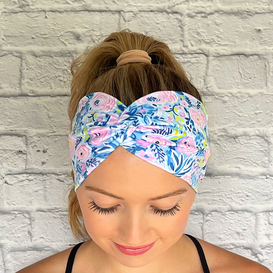 Woman with hair in curled ponytail wearing wide, twisted headband with blue, pink, and green floral print.