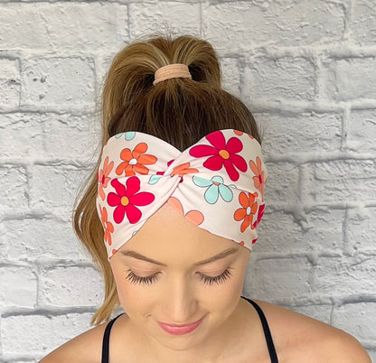 Woman wearing a colorful floral headband against a white brick wall.