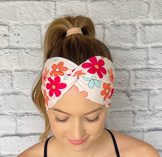 Woman wearing a colorful floral headband against a white brick wall.