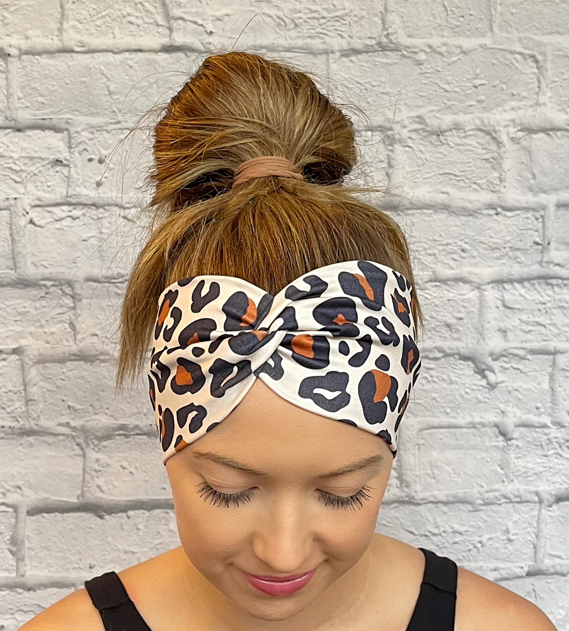 Woman with hair in bun wearing wide, twisted headband in brown and black cheetah print.