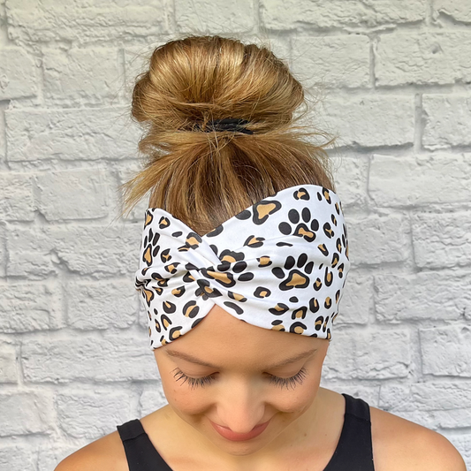 Woman with hair in bun wearing wide, white, twisted headband with brown and black dog paws and cheetah print. 