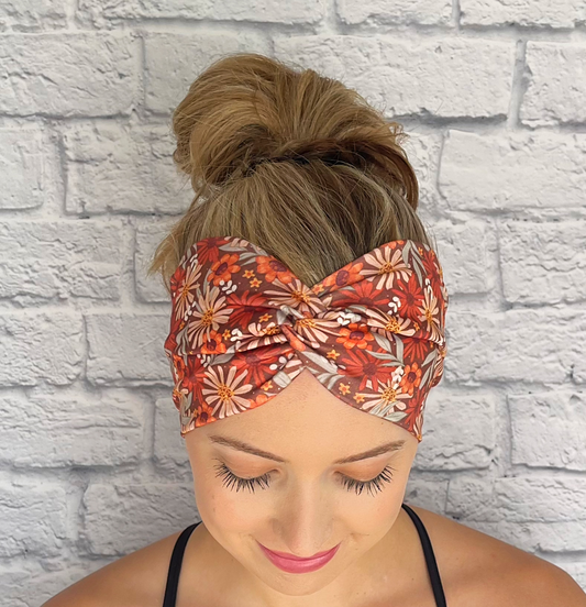 Woman with hair in bun wearing wide, twisted, brown, red, orange, and white floral print headband.