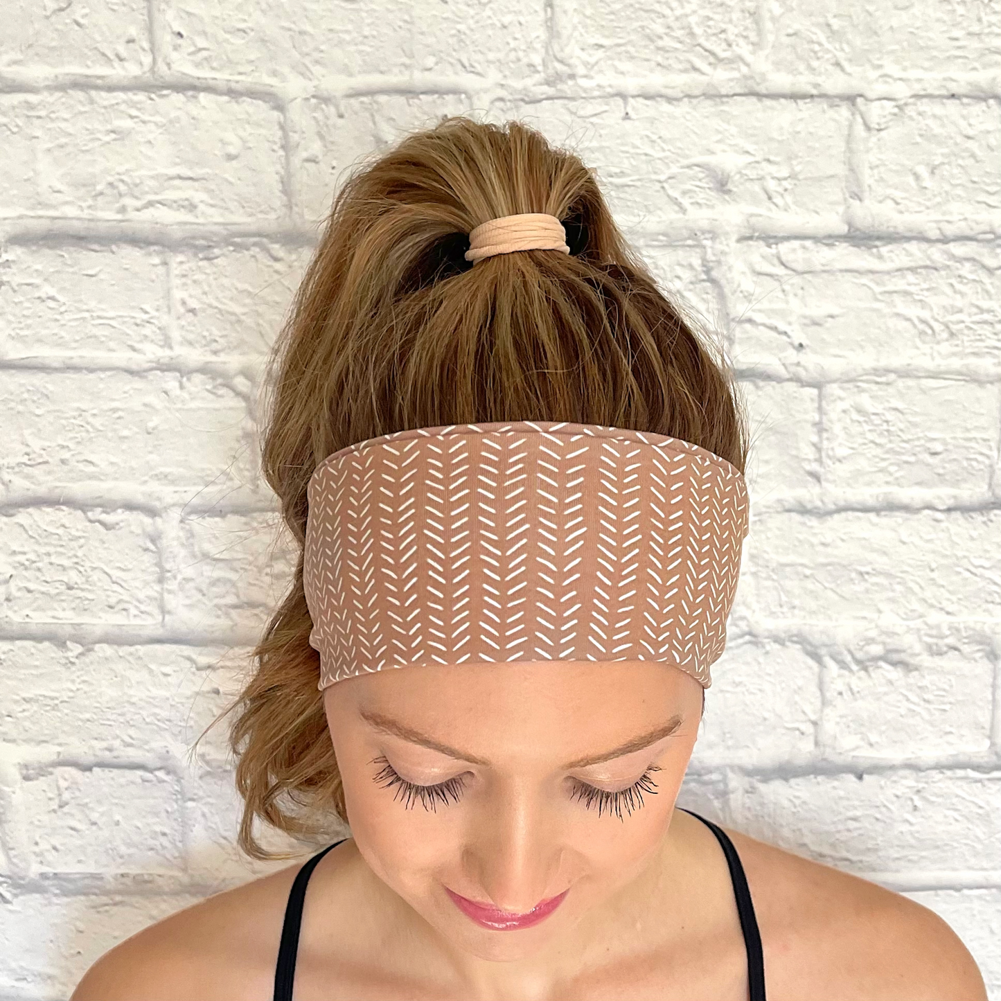 Woman with hair in ponytail wearing light brown headband with small white lines printed throughout headband.