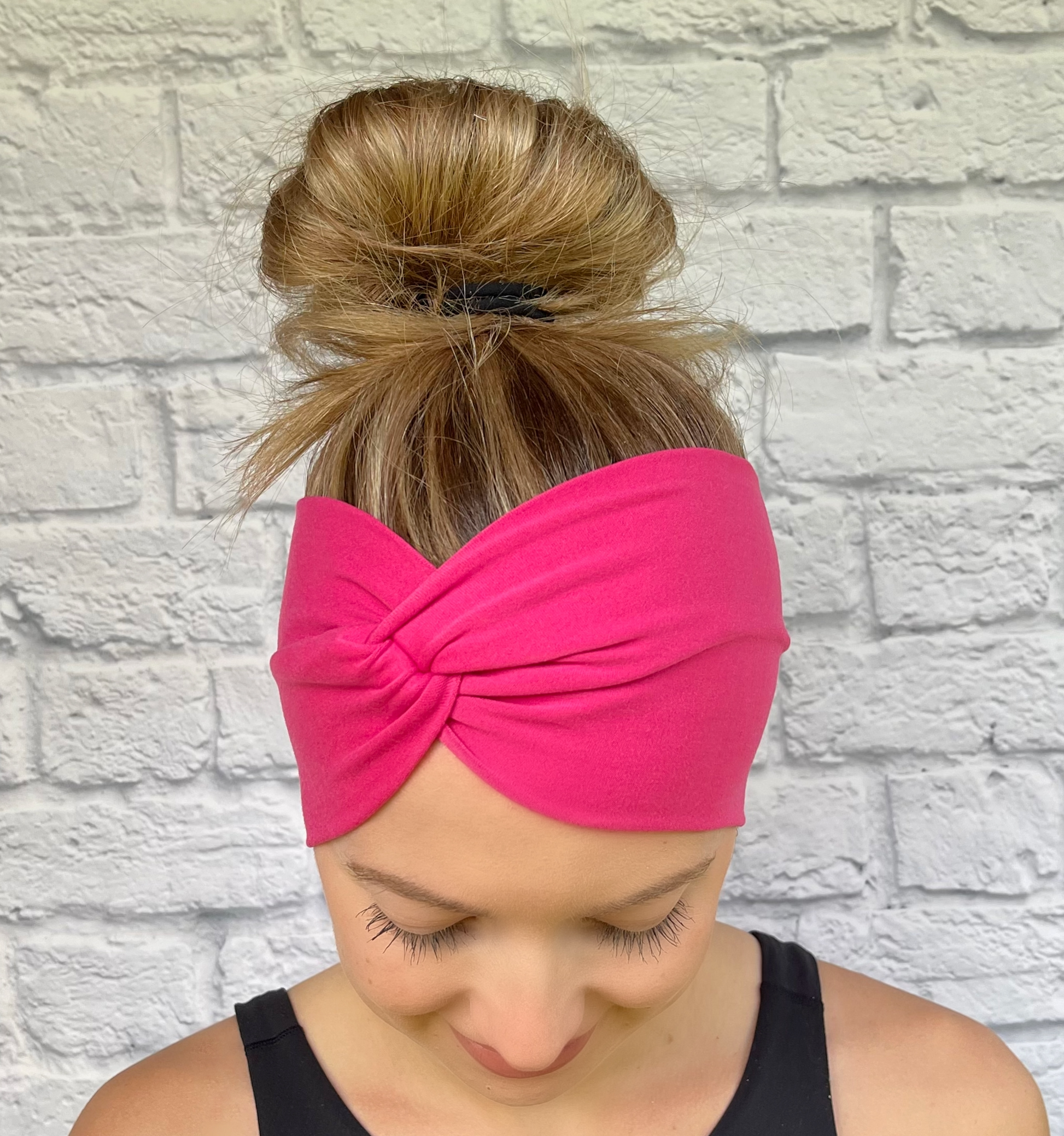 Woman with hair in bun wearing wide, twisted headband in bubblegum, bright pink color.