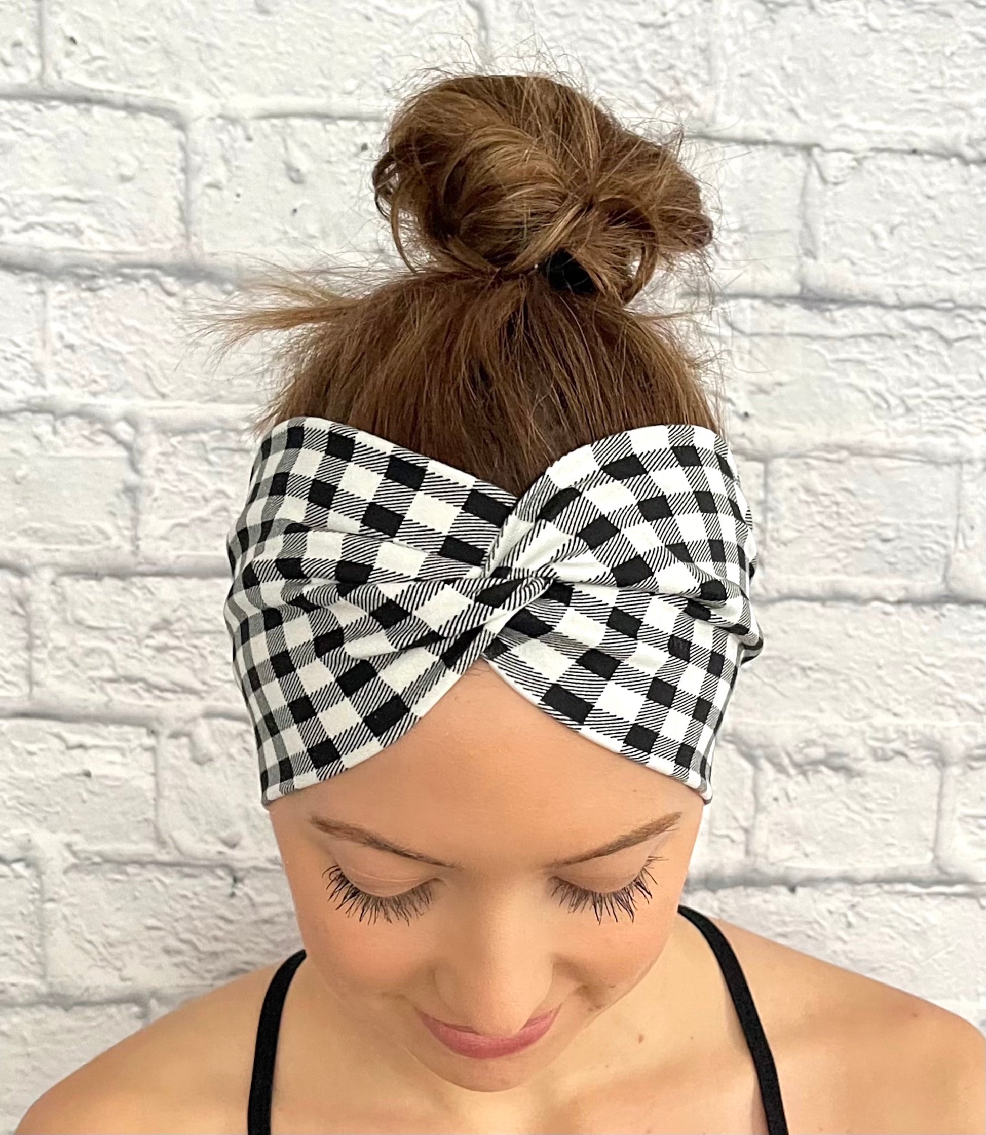 Woman with hair in bun wearing wide, twisted headband in black and white buffalo plaid print.